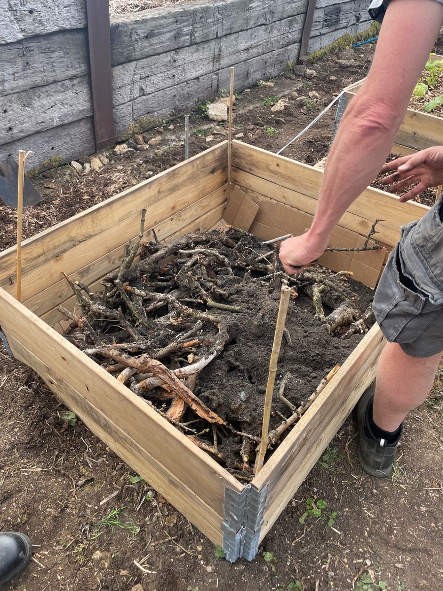 Hands arranging branches and soil inside a raised bed