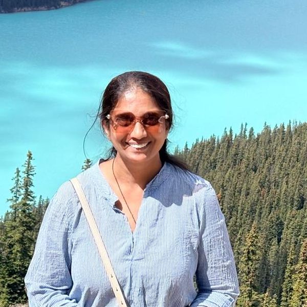 Neema, workshop facilitator, smiling in front of a turquoise mountain lake